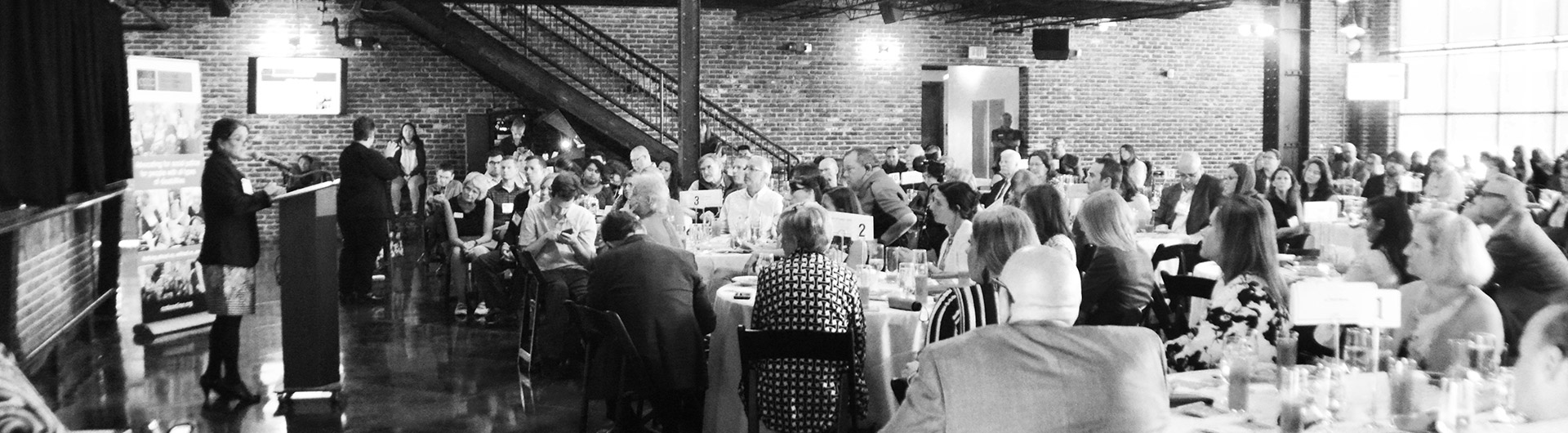 Black and white image of people seated at a CCDC event listening to a speaker