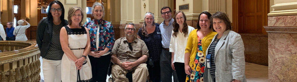 Group of people in the capitol standing supportively around a man in a wheelchair